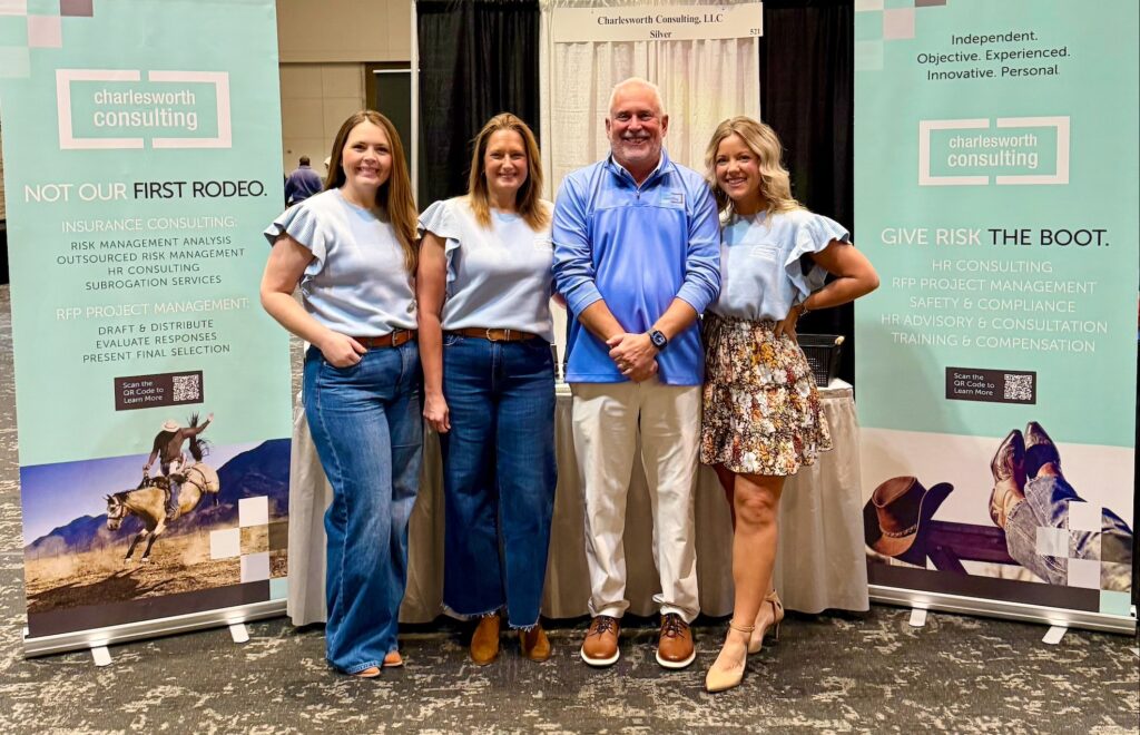 Four people stand smiling between two Charlesworth Consulting banners at an indoor event. 